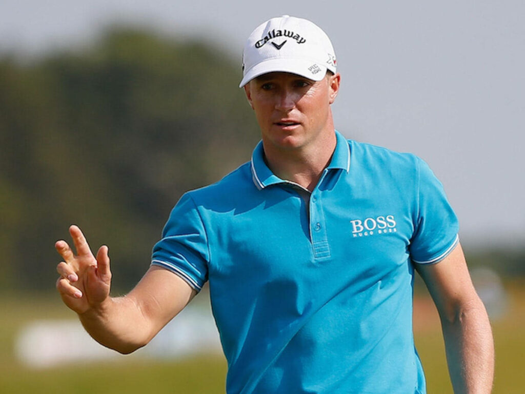 Alex Norén golfing in blue polo and white cap gesturing on course with wallpaper background