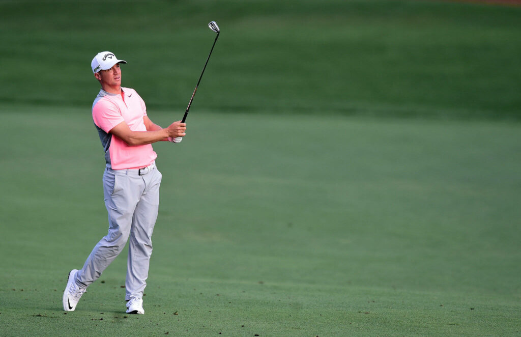 Alex Norén mid-swing golf shot pink shirt light gray pants green golf course background Wallpaper