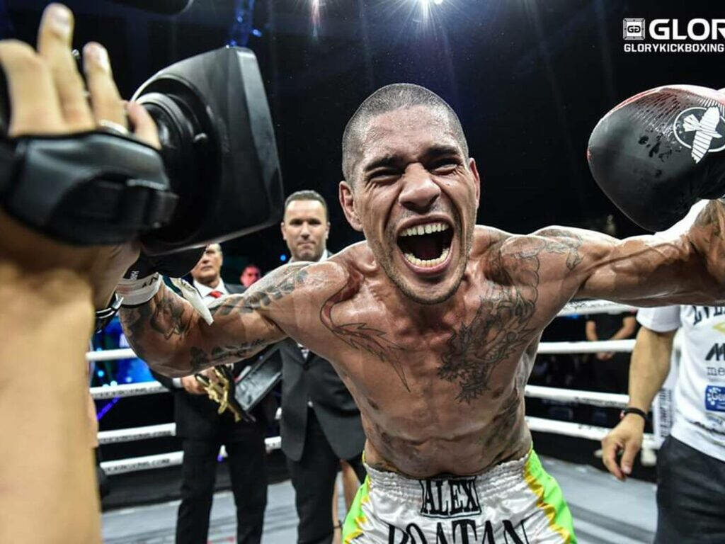 Alex Pereira celebrates victory energetically inside boxing ring with wallpaper background scene