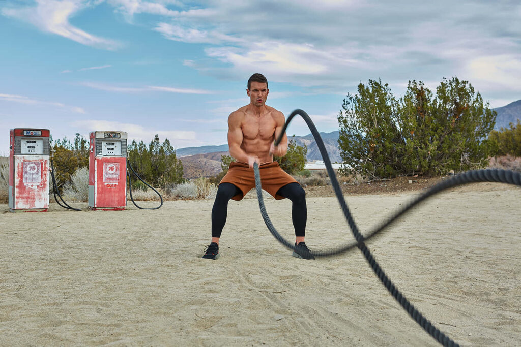 Alex Russell intense outdoor battle rope workout by old gas pumps rugged landscape background Wallpaper