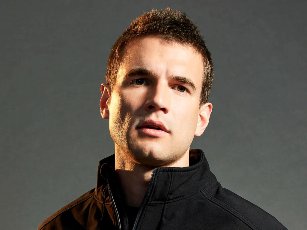 Portrait of Alex Russell in black jacket with intense focused expression on dark background Wallpaper