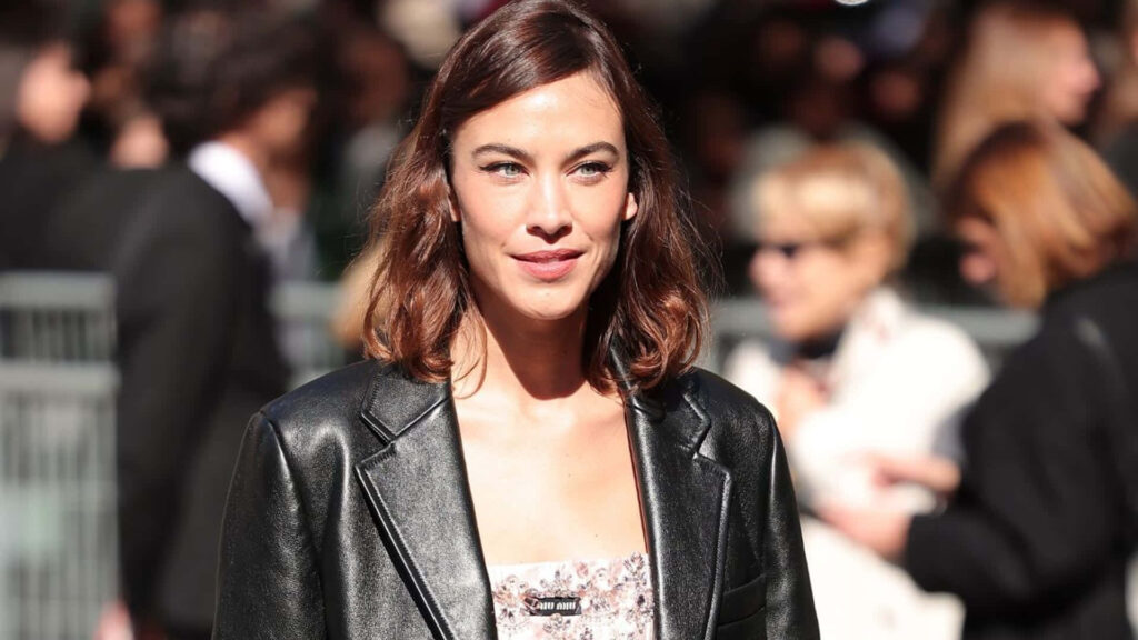 Alexa Chung in sleek leather jacket and patterned top at stylish event with blurred crowd background Wallpaper
