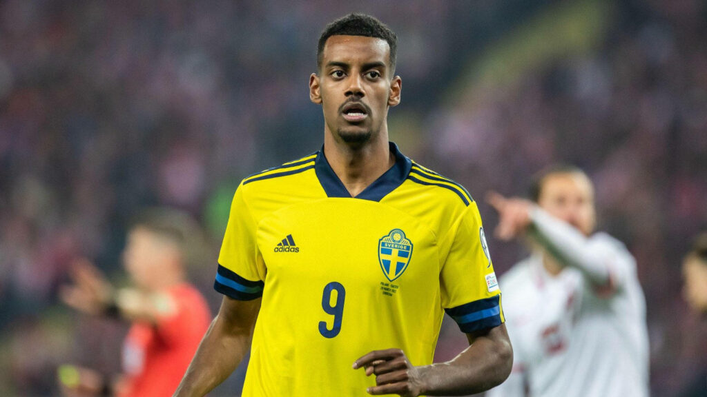 Alexander Isak in Sweden jersey focused on field serious expression blurred stadium background Wallpaper