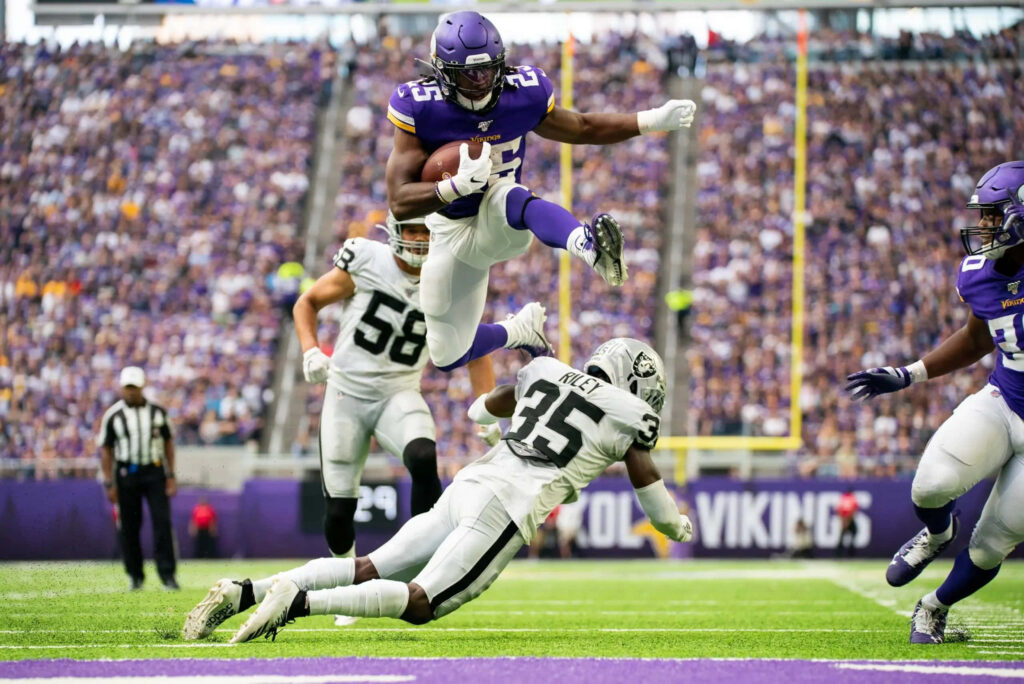 Alexander Mattison jumps over defender in intense football action dynamic athletic wallpaper background