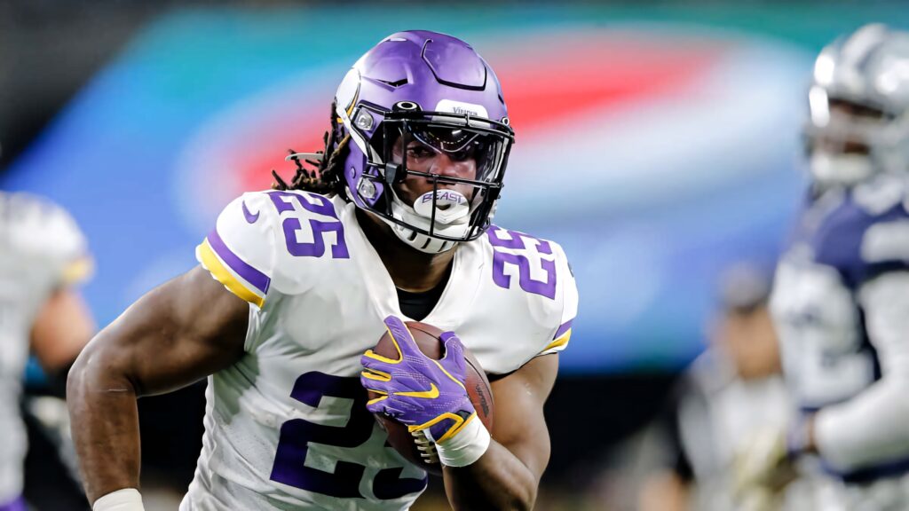 Alexander Mattison runs with football in Minnesota Vikings uniform during intense game action Wallpaper