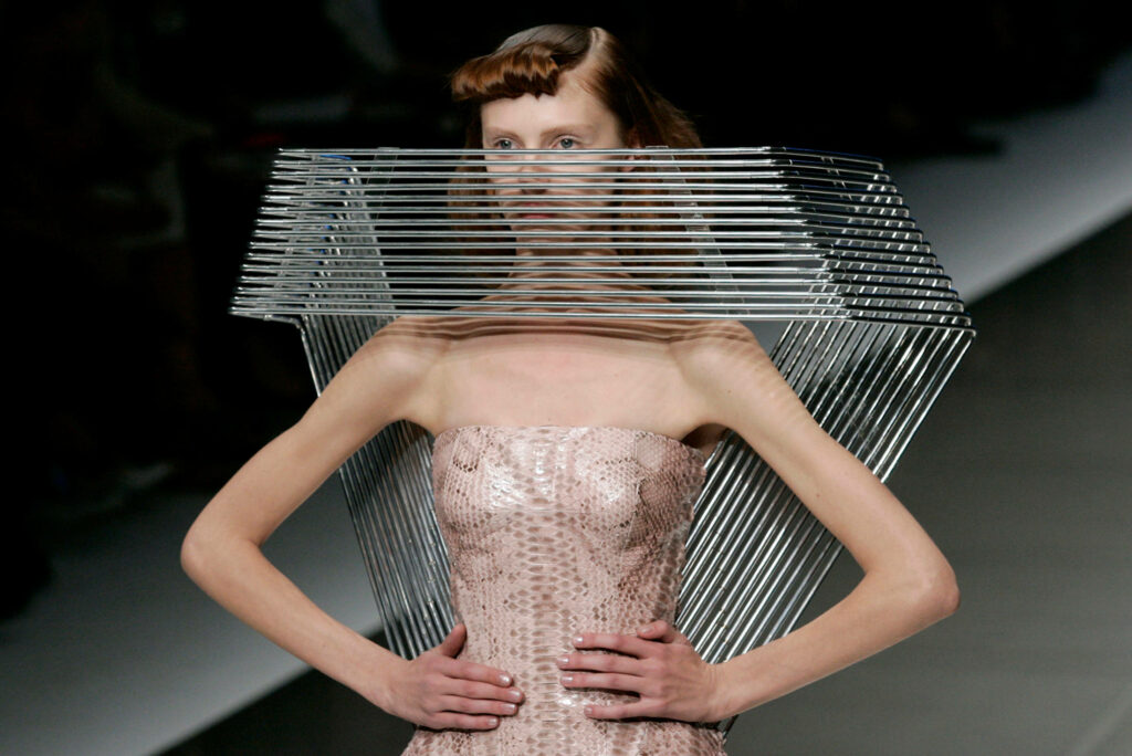 Alexander McQueen runway model wearing avant-garde metallic cage face mask and textured dress wallpaper