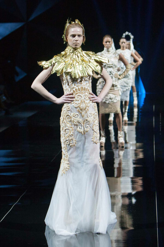 Model in Alexander McQueen Goddess Dress with gold details and elaborate collar on runway background Wallpaper