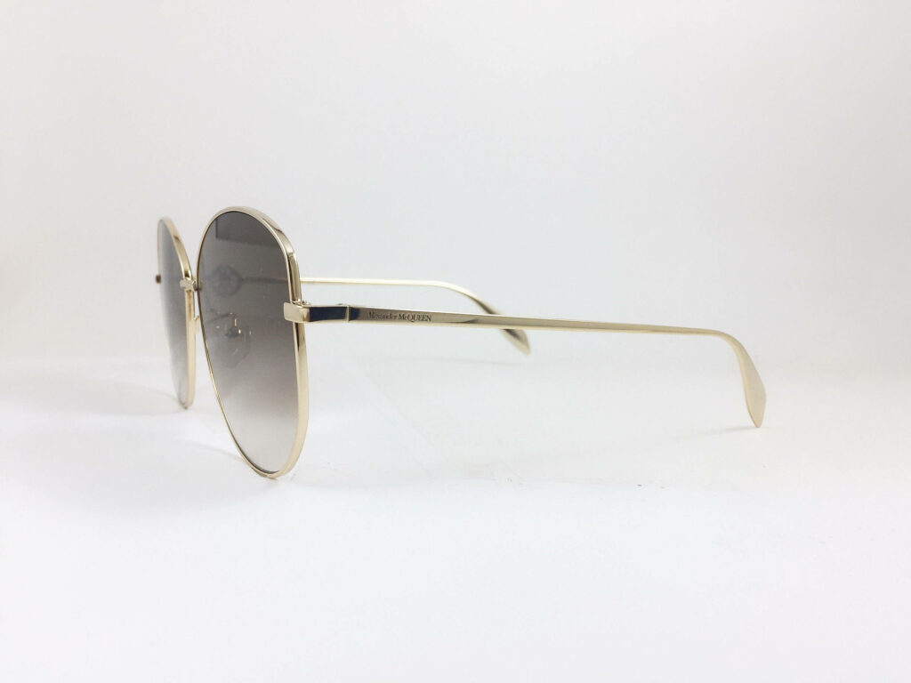 Alexander McQueen gold rimmed sunglasses with round lenses minimalist design on white background Wallpaper