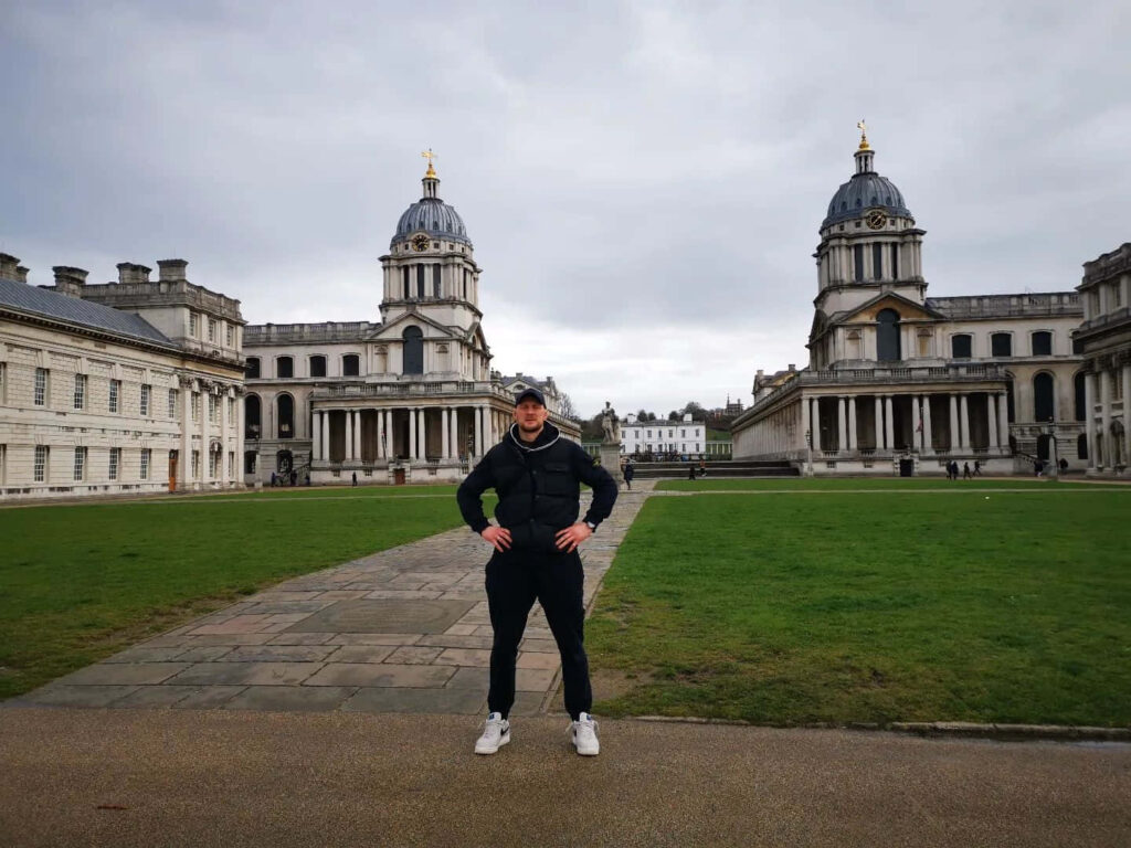 Alexander Volkov poses confidently with grand European historic buildings and lush lawn background Wallpaper