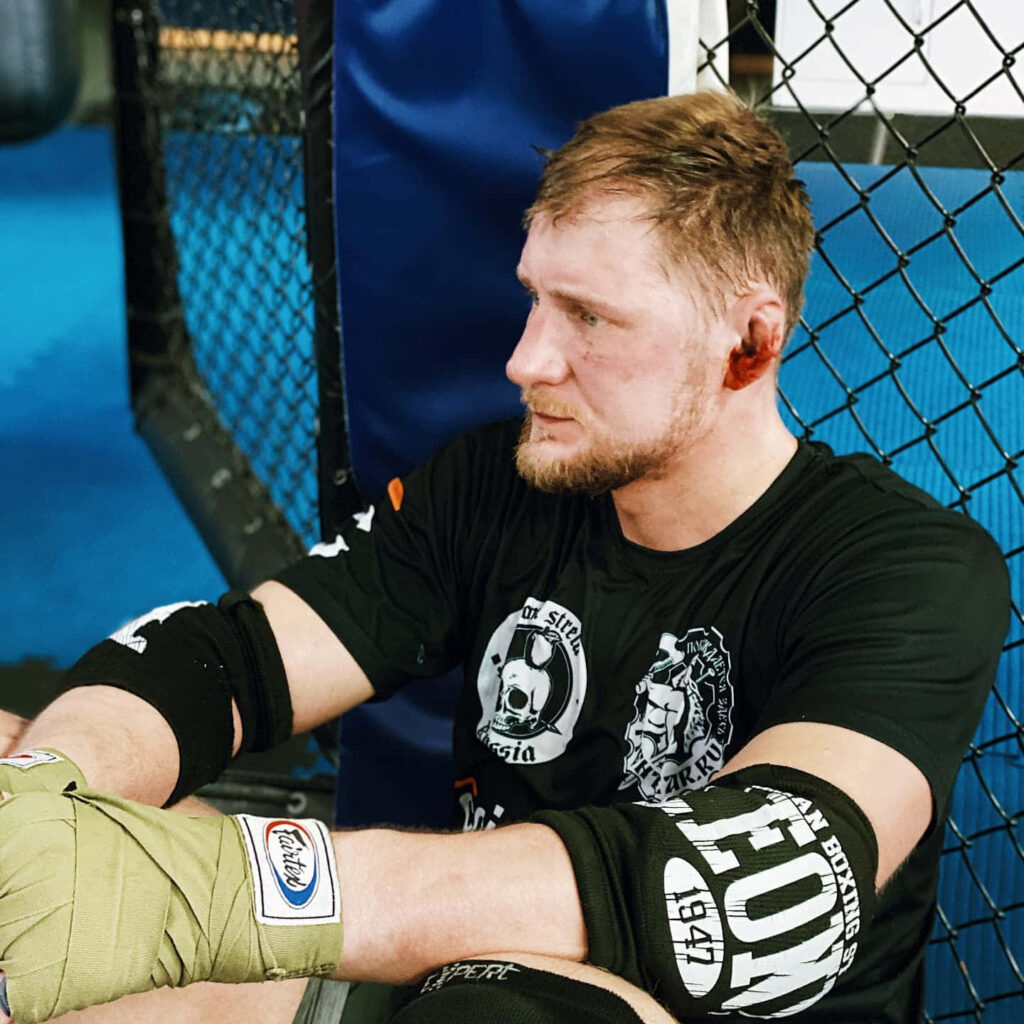 Alexander Volkov focused and resilient with bandaged hands sitting against cage after intense fight Wallpaper