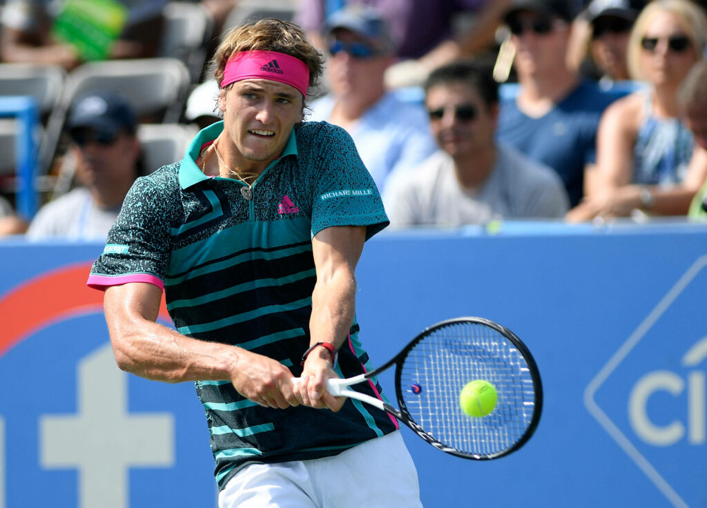 Alexander Zverev focused returning tennis shot during match with cheering fans in stands background Wallpaper