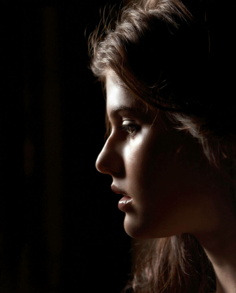 Side profile portrait of Alexandra Daddario with soft lighting on dark artistic wallpaper background
