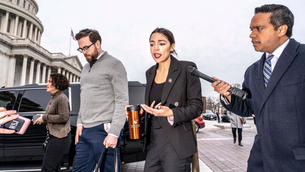 Representative Alexandria Ocasio Cortez speaking to reporters outside Capitol with microphones and cameras Wallpaper