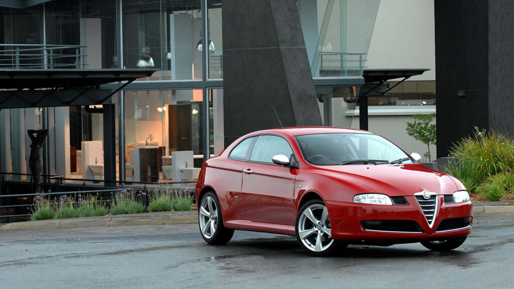 Red Alfa Romeo GT parked on scenic road with modern architecture showcasing sporty design Wallpaper