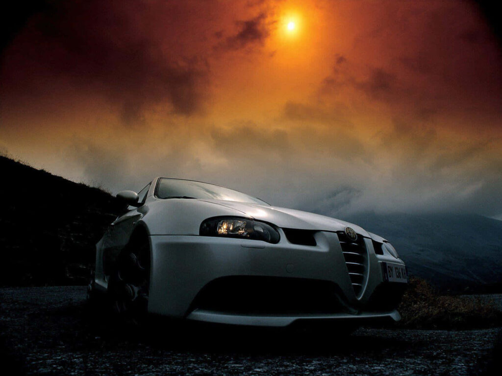 Alfa Romeo GT on scenic road with glowing sun misty mountains and dramatic sky wallpaper background