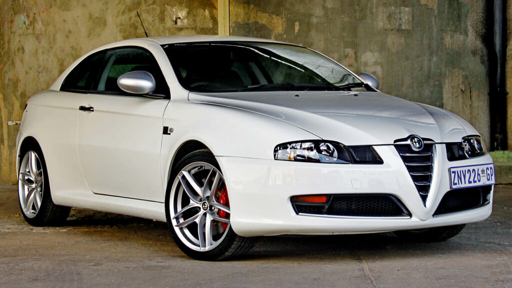 Silver Alfa Romeo GT sports car parked against rugged concrete wall wallpaper background