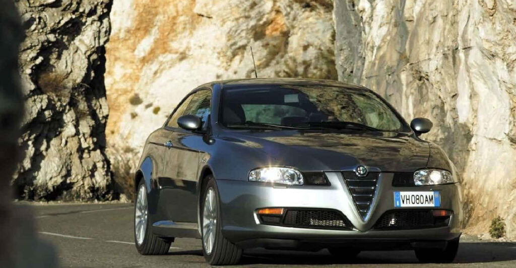Alfa Romeo GT speeding on winding mountain road with rocky cliffs and sleek sporty design Wallpaper