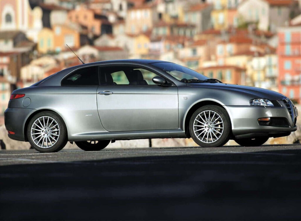 Sleek Alfa Romeo GT on open road with vibrant blurred cityscape showcasing sporty design Wallpaper