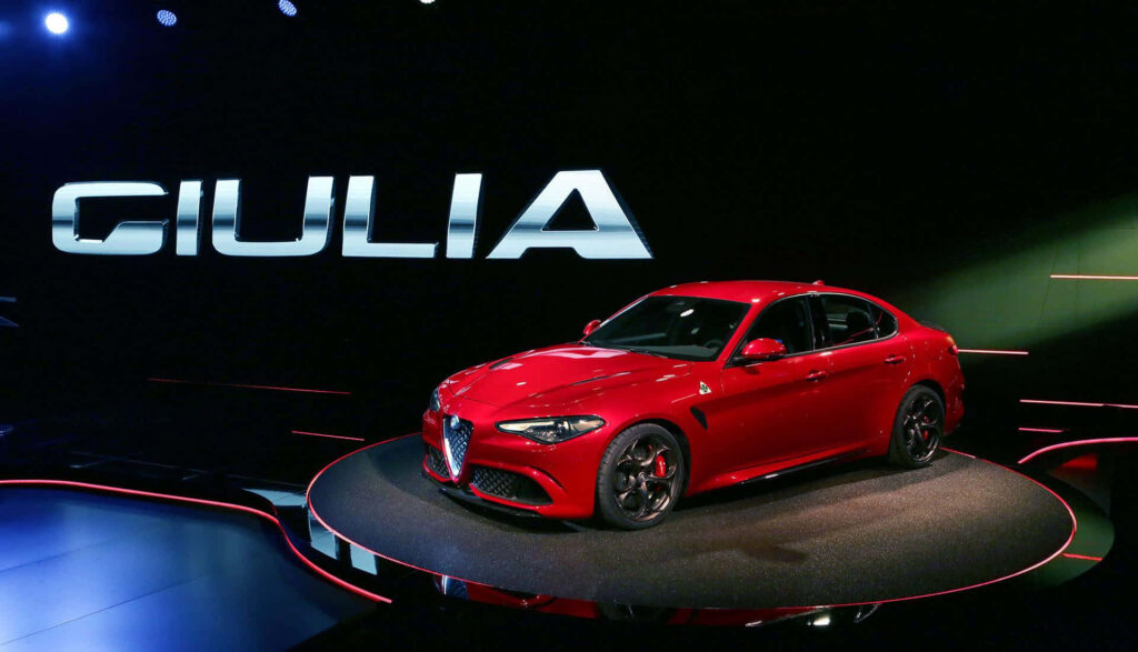 Red Alfa Romeo Giulia sports car on stage with bold GIULIA logo and dramatic lighting backdrop Wallpaper