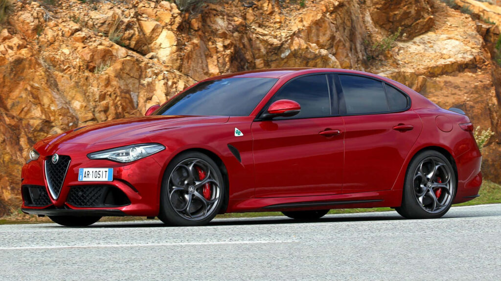 Red Alfa Romeo Giulia driving on scenic road with rocky terrain background wallpaper image
