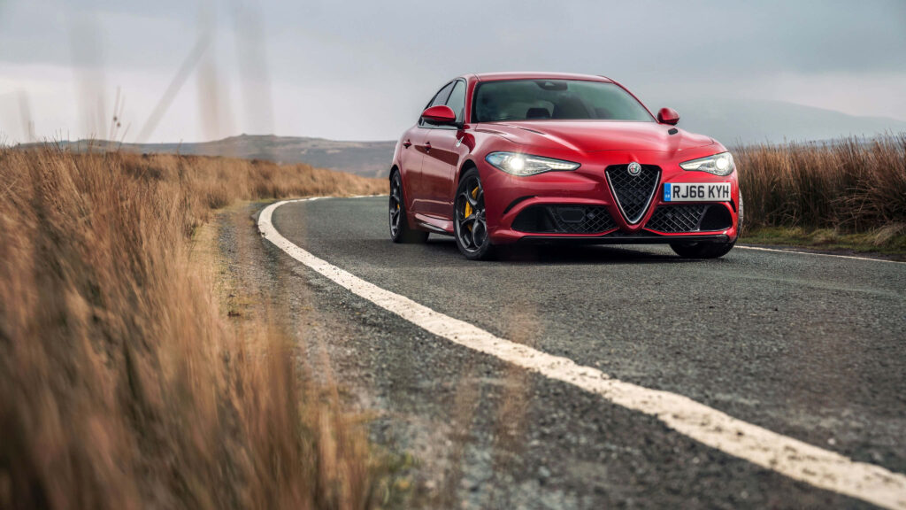 Alfa Romeo Giulia speeding on winding country road showcasing Italian car design elegance Wallpaper