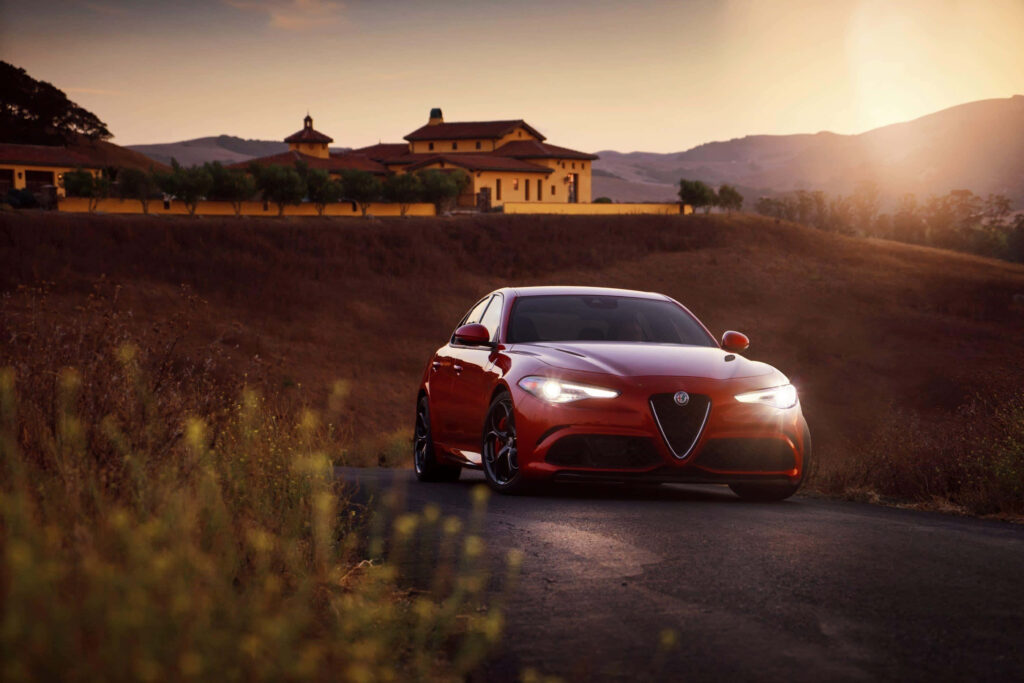Alfa Romeo Giulia speeding on scenic sunset country road showcasing elegance and performance Wallpaper