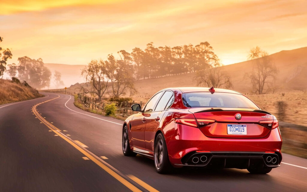 Alfa Romeo Giulia speeding on winding countryside road at sunset scenic driving wallpaper background
