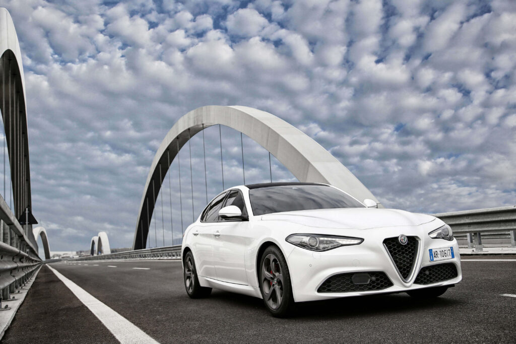Alfa Romeo Giulia on scenic road with dramatic clouds and modern bridge arches background Wallpaper