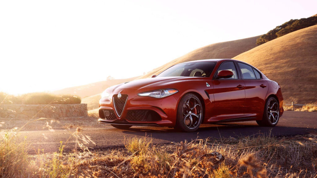 Alfa Romeo Giulia on scenic road with golden sunlight and rolling hills wallpaper background