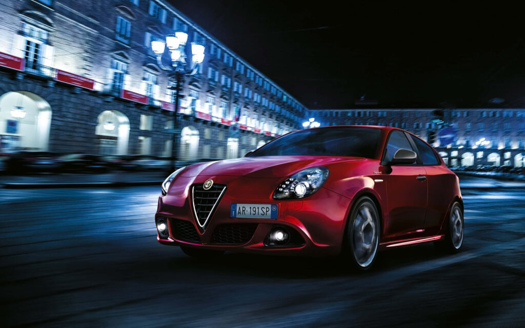 Alfa Romeo Giulietta speeding through vibrant cityscape at night showcasing sporty and sleek design Wallpaper