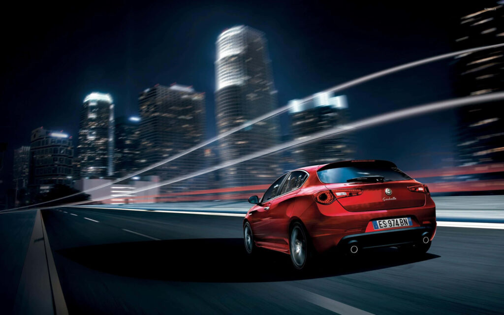 Alfa Romeo Giulietta speeding at night in modern cityscape with blurred lights wallpaper background