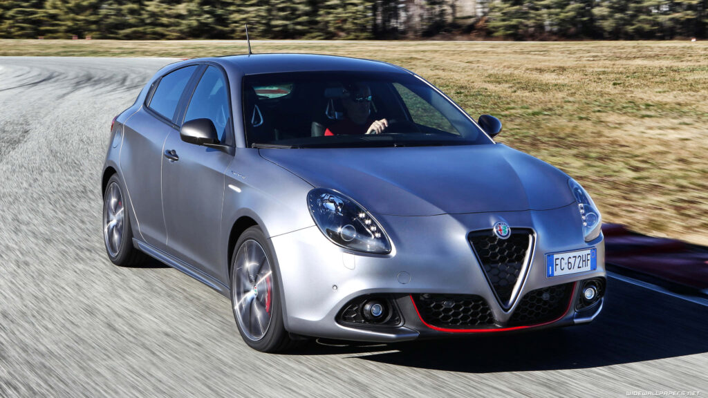 Alfa Romeo Giulietta in motion on curving road with sporty Italian design and natural backdrop Wallpaper