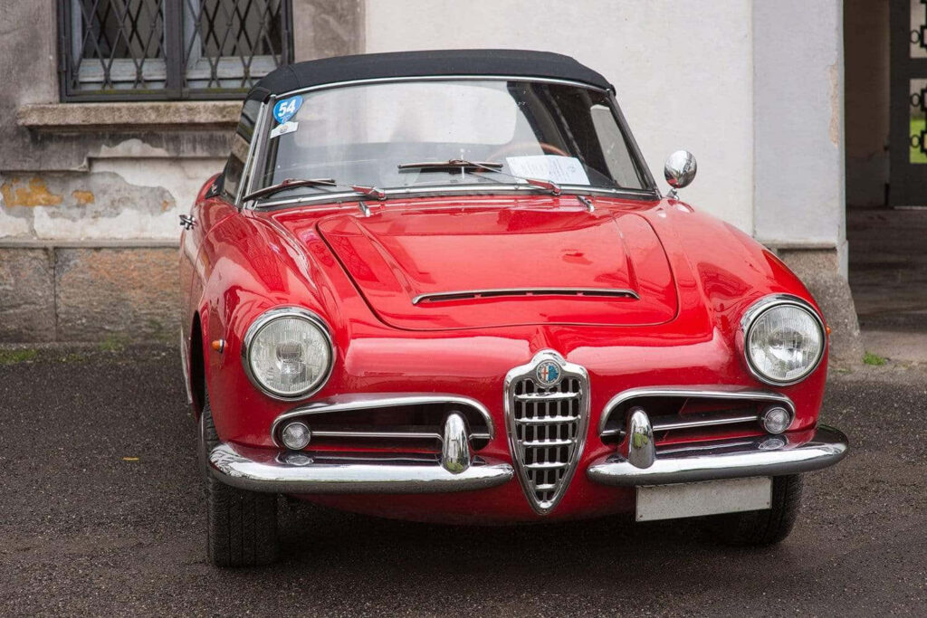 Red Alfa Romeo Spider vintage car with classic curves against urban cityscape background wallpaper