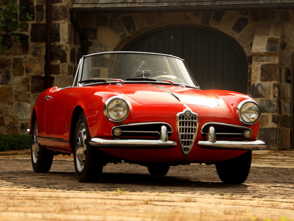 Red Alfa Romeo Spider convertible gleaming against rustic stone wall vintage car wallpaper background