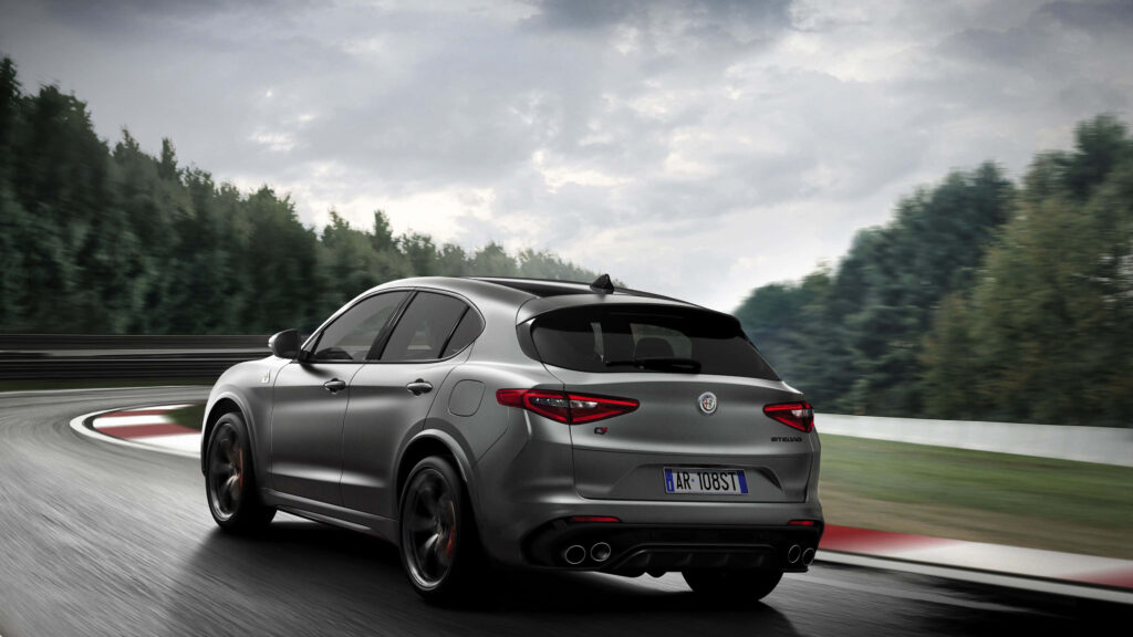 Alfa Romeo Stelvio driving on winding mountain road with lush green trees and cloudy sky wallpaper