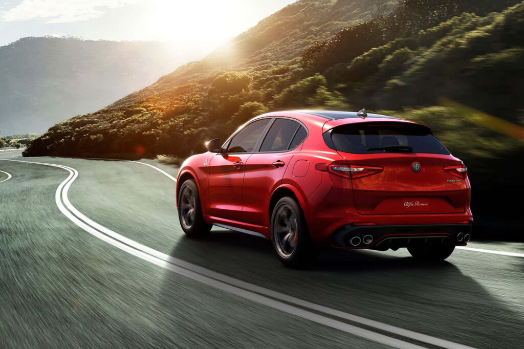 Alfa Romeo Stelvio driving on winding mountain road bathed in golden sunlight scenic wallpaper