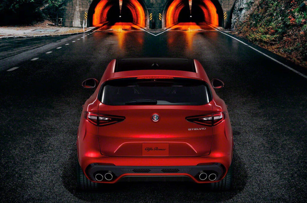 Alfa Romeo Stelvio rear view driving towards lit tunnels on open road showcasing sporty design Wallpaper