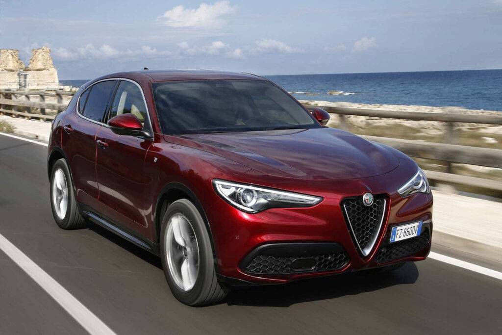Glossy red Alfa Romeo Stelvio driving on scenic mountain road showcasing performance and elegance Wallpaper