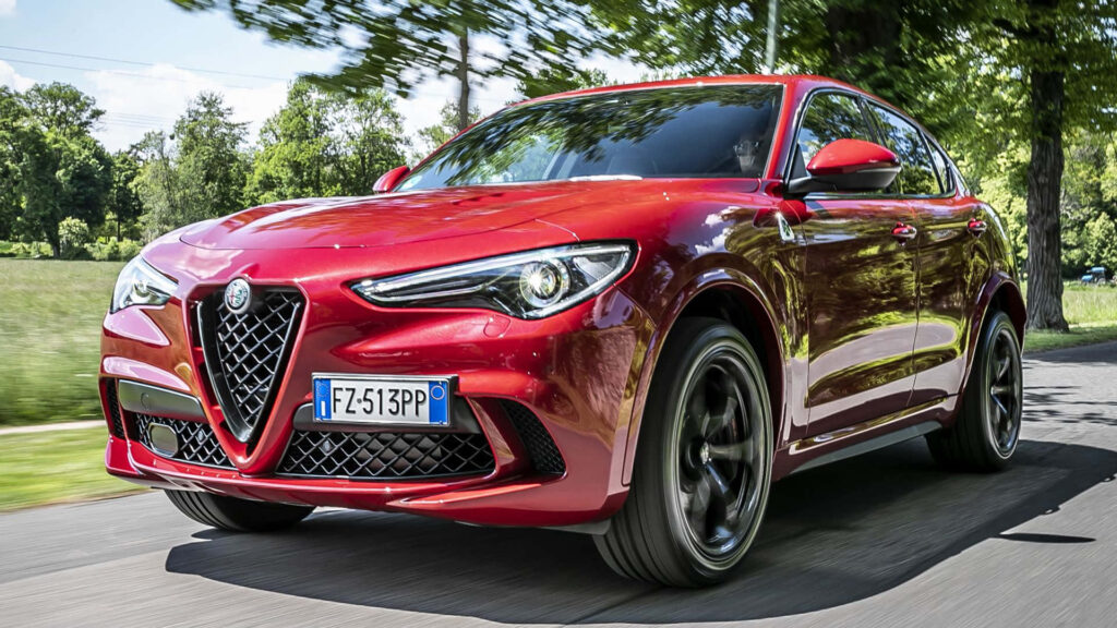 Alfa Romeo Stelvio in bold red driving on scenic tree-lined road sporty luxury SUV wallpaper