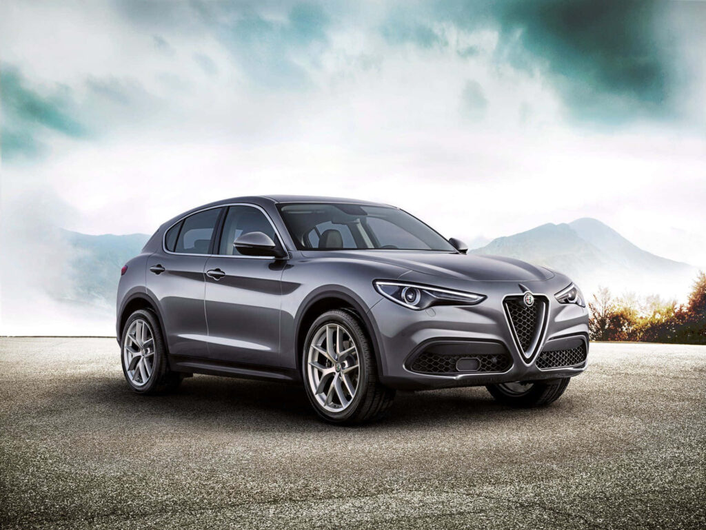 Alfa Romeo Stelvio SUV parked in scenic wilderness with misty mountains and dramatic sky wallpaper