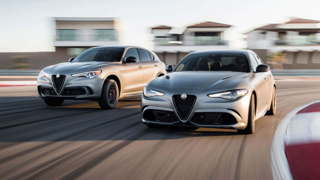 Alfa Romeo Stelvio and sedan driving on winding road with modern houses blurred background wallpaper
