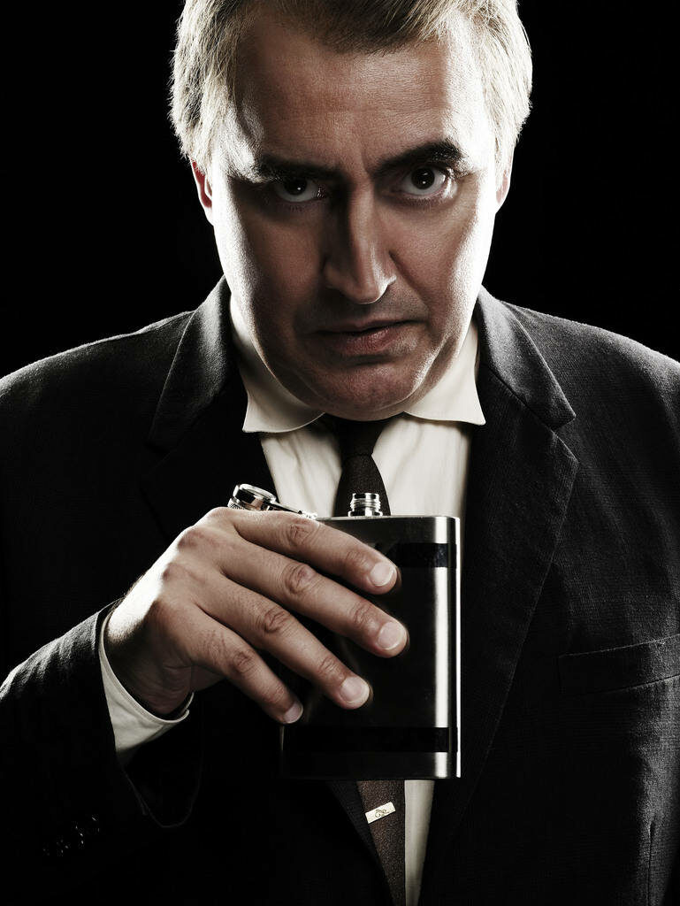 Alfred Molina in dark suit holding flask with intense expression in moody The Company wallpaper