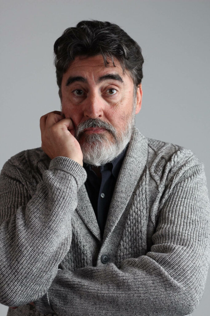 Alfred Molina thoughtful portrait in gray cardigan on neutral background wallpaper image
