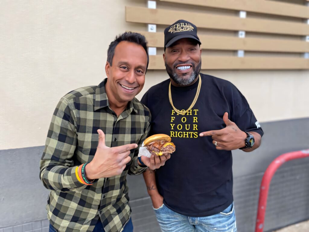 Ali Khan and Bun B smiling outdoors holding smashed burger casual streetwear vibrant wallpaper