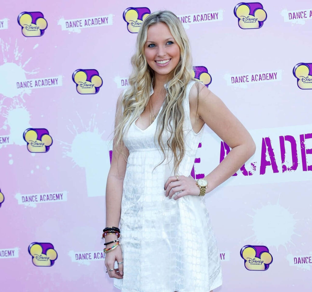 Alicia Banit smiling at Dance Academy event with Disney and Dance Academy logo backdrop wallpaper