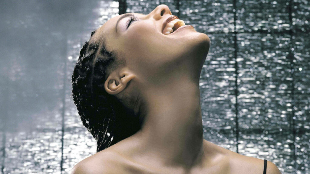 Alicia Keys with radiant box braids and natural beauty against softly lit textured wallpaper background