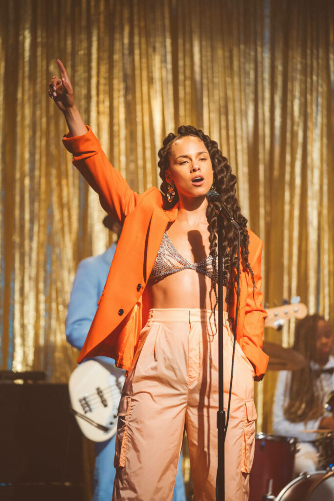 Alicia Keys singing So Done on stage in orange jacket with golden glittering backdrop wallpaper