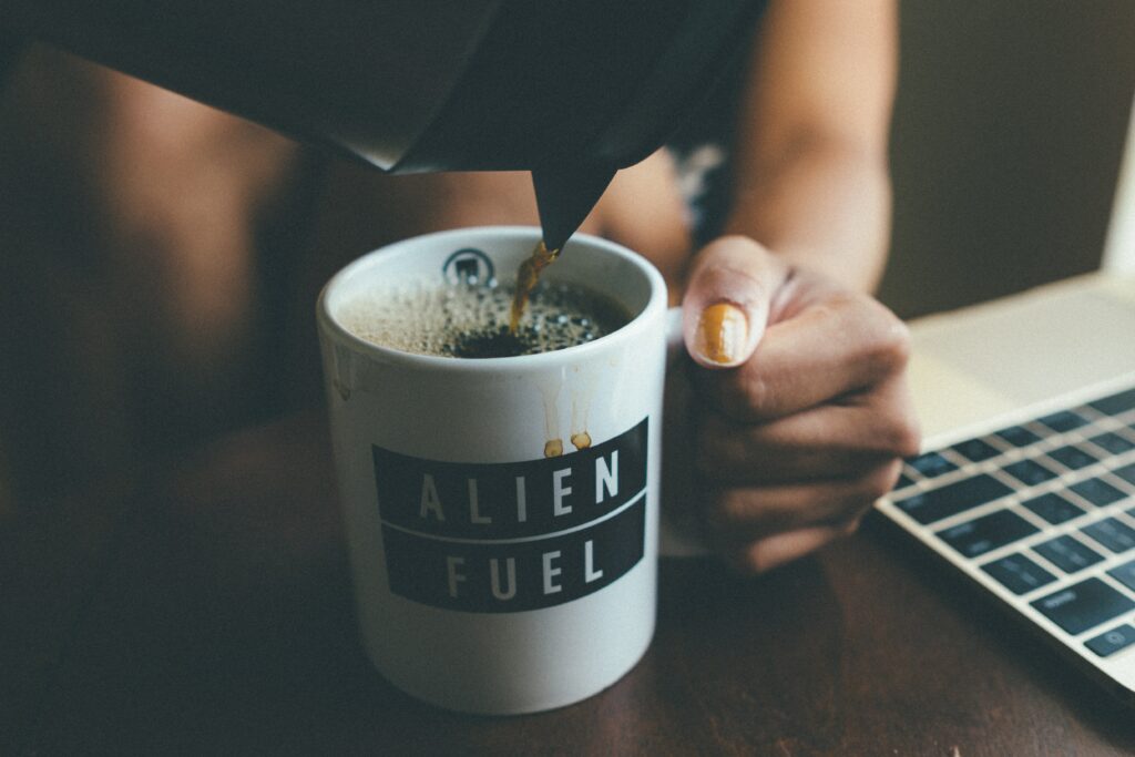 Close-Up: Alien Fuel Coffee Mug on Wooden Table with Laptop Wallpaper