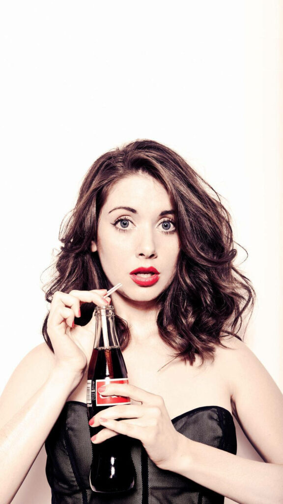 Alison Brie with wide eyes red lips sipping classic Coca Cola bottle playful retro wallpaper background