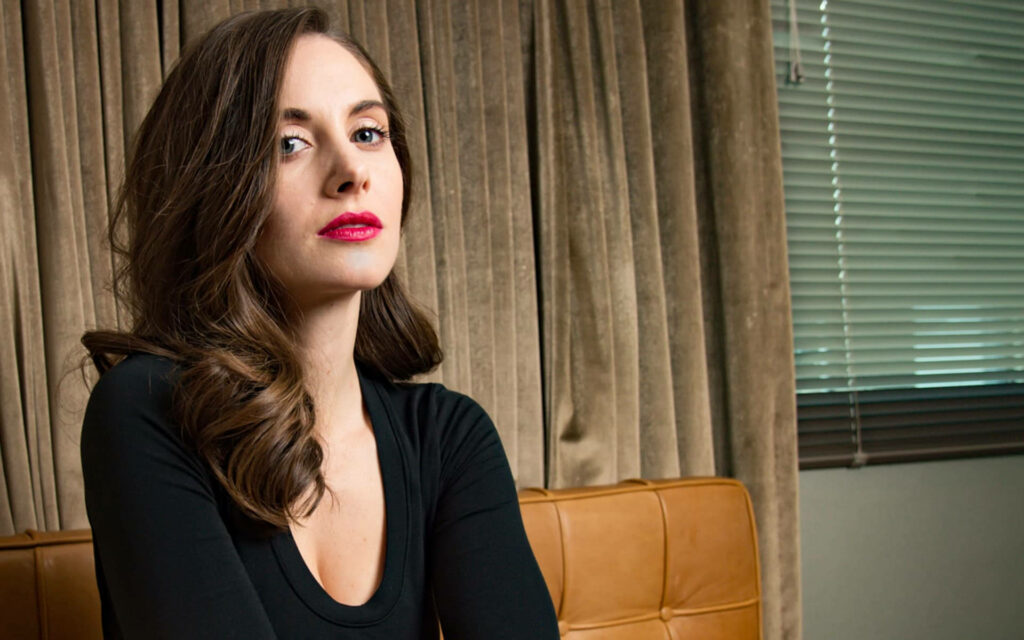 Alison Brie side profile wallpaper black top soft wavy hair confident expression neutral curtains